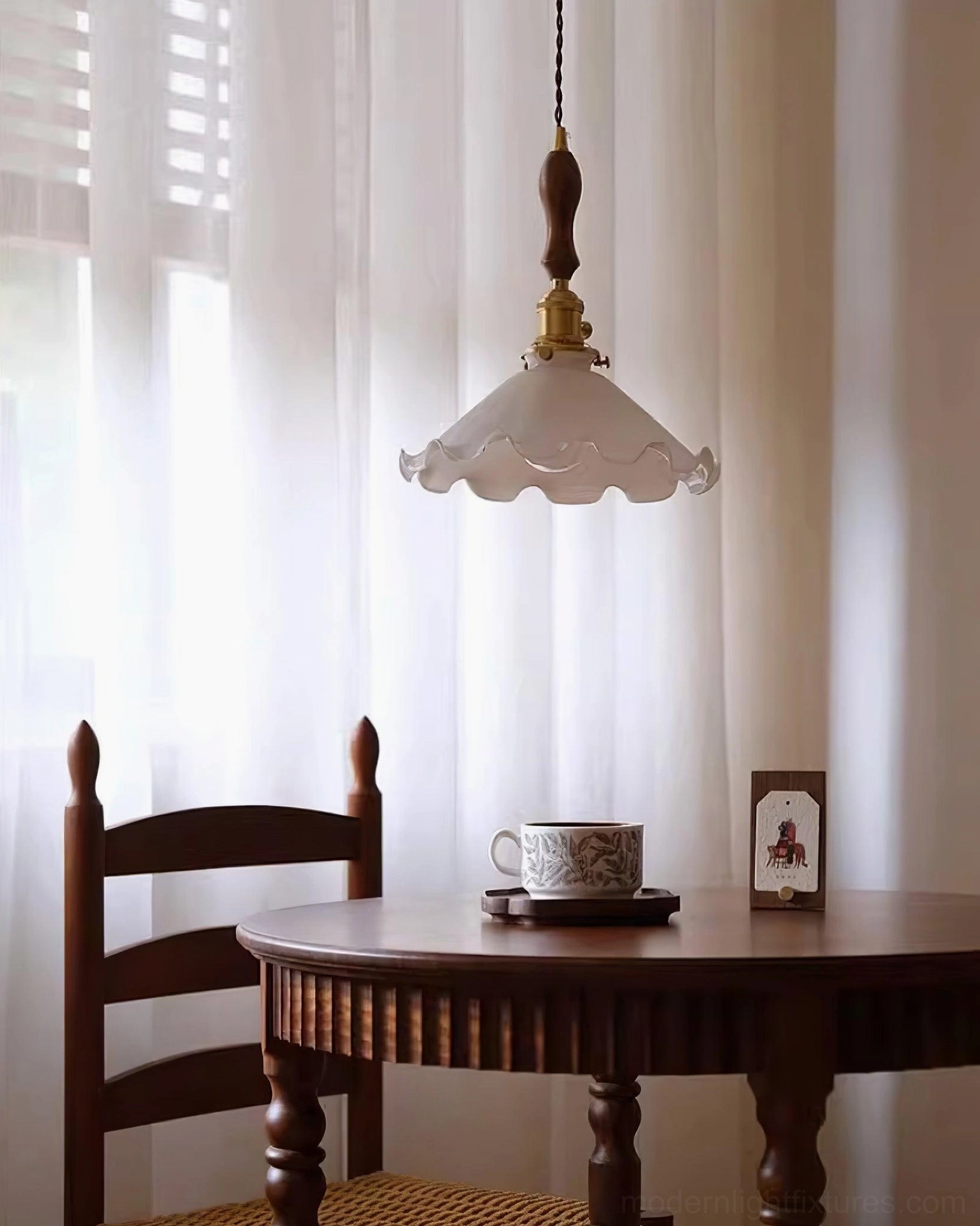 Pale pink ruffled glass pendant light over dining table with walnut wood and brass hardware