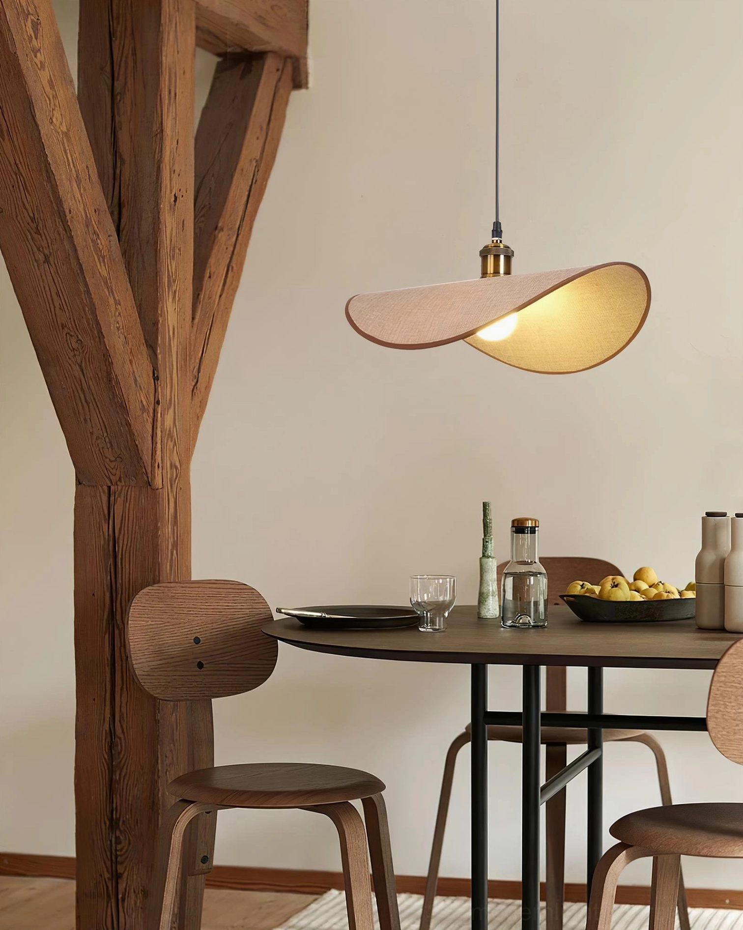 Single handcrafted pendant lamp with light fabric shade above rustic farmhouse dining table with wooden beam ceiling