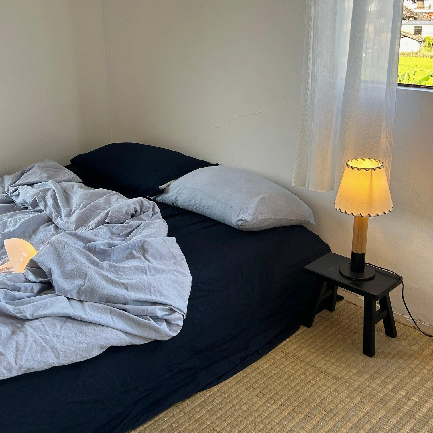 Warm glowing rustic table lamp on dark wood nightstand in bedroom corner with sunny window light