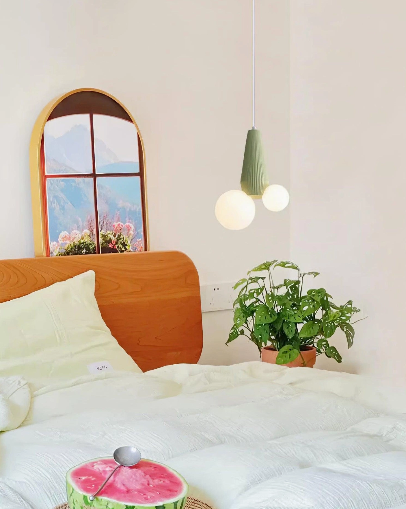 Sage green ribbed pendant fixture with frosted glass globes suspended above modern bed with arched window