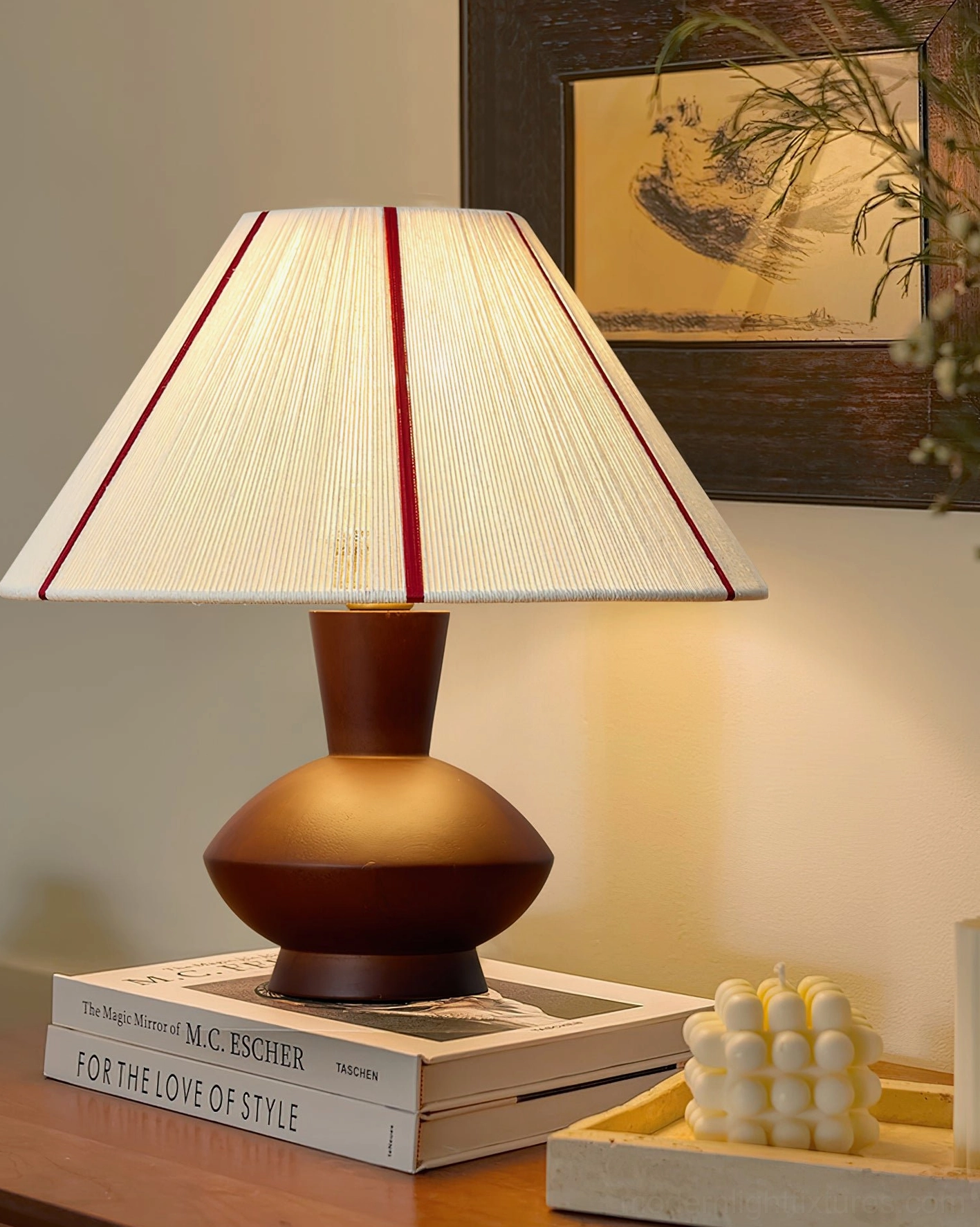 Sandia mid-century table lamp beside stacked books and decorative candles, illuminated warm glow, cozy reading area and home library setting