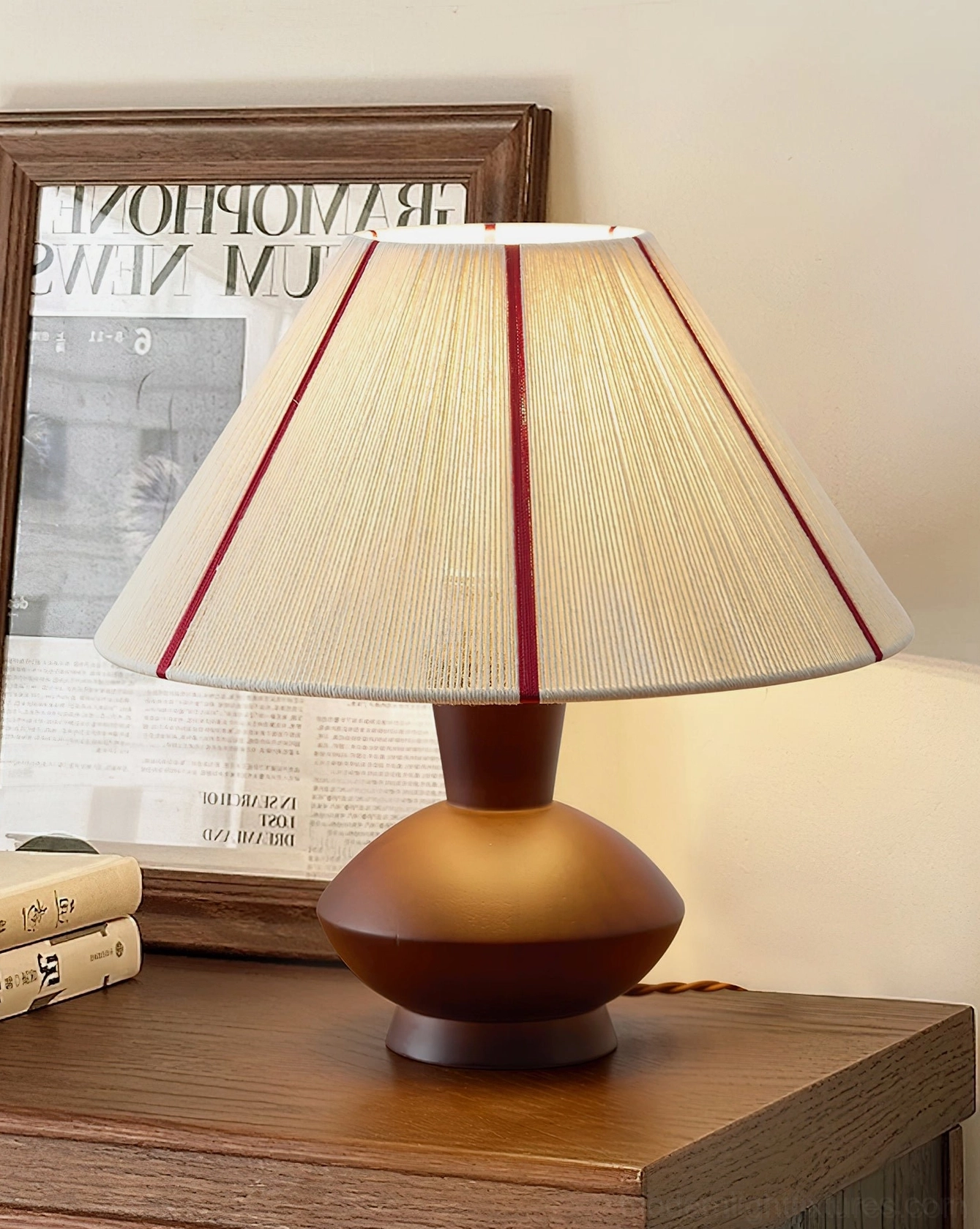 Sandia hand-woven table lamp on wooden side table with newspaper print and stacked books, reading nook corner setup, functional lighting
