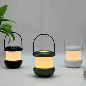 Sarina portable LED lantern in three color options - white, black, and deep green matte finishes - three-quarter view with plants