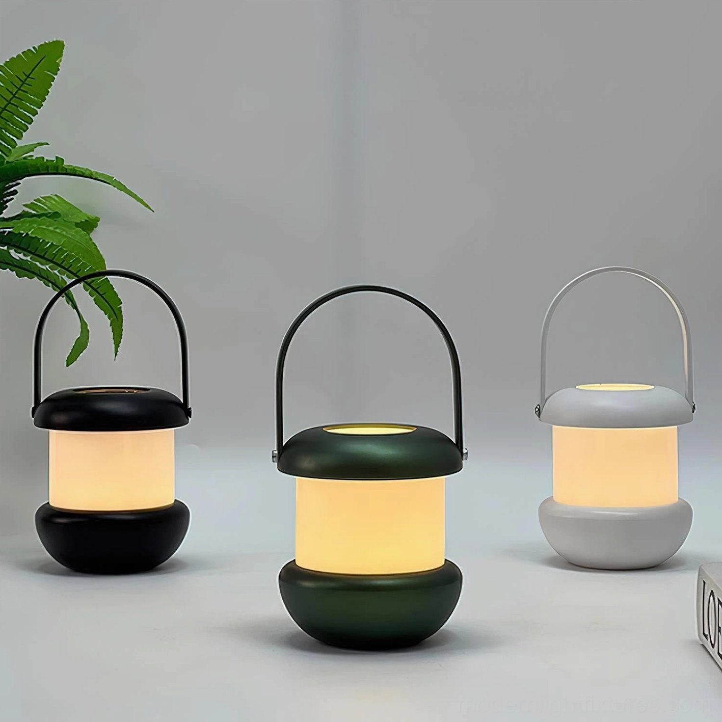 Sarina portable LED lantern in three color options - white, black, and deep green matte finishes - three-quarter view with plants