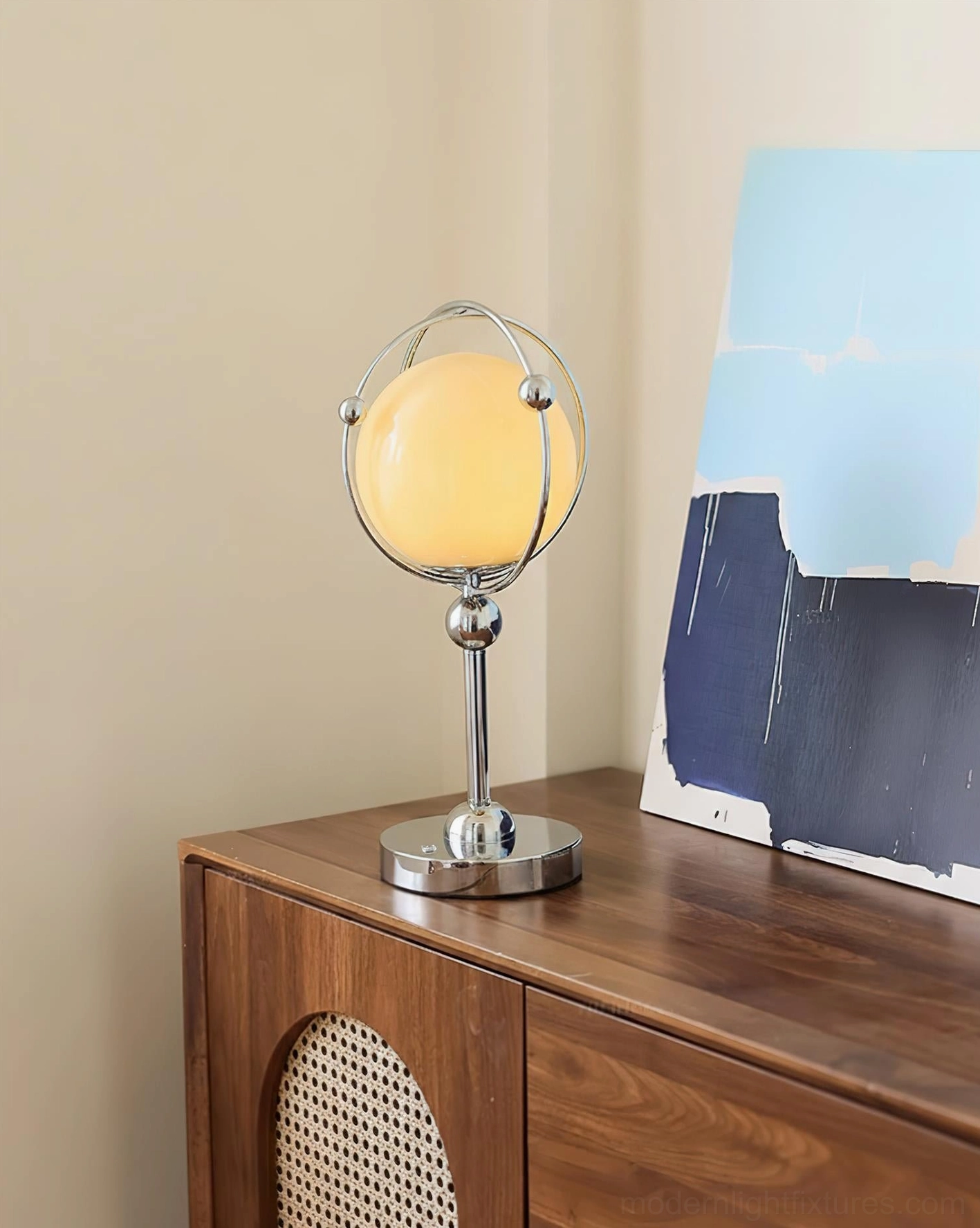 Saturn Hoop Table Lamp with warm glow on rattan panel wooden cabinet paired with abstract painting