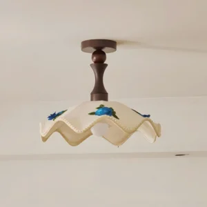Overhead close-up detail of wavy fabric ceiling light showing scalloped edges, floral embroidery, and dark turned wood mounting canopy