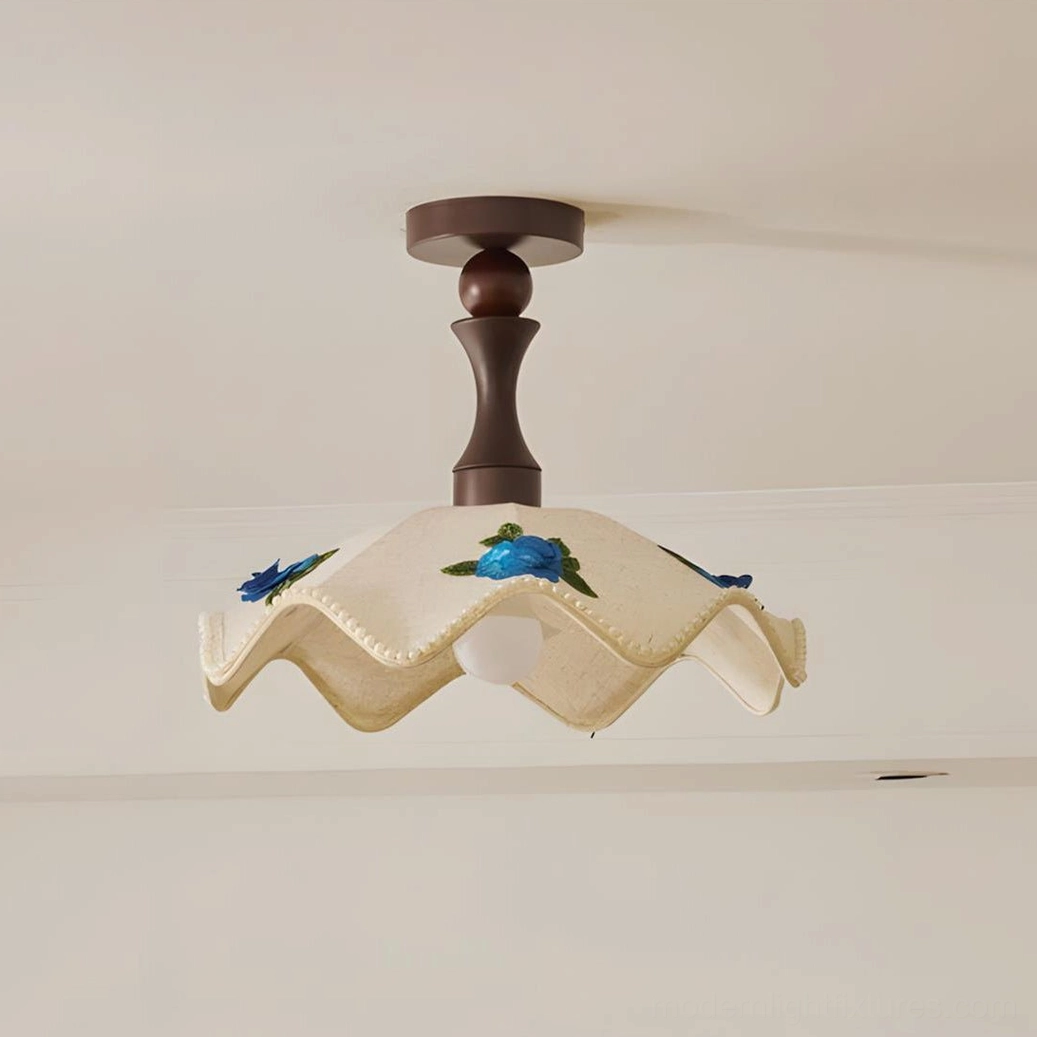 Overhead close-up detail of wavy fabric ceiling light showing scalloped edges, floral embroidery, and dark turned wood mounting canopy