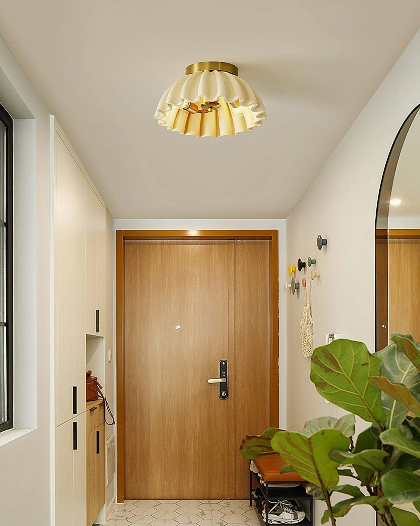 Front view of ruffled ceiling light fixture in residential entryway with wooden door and green plant