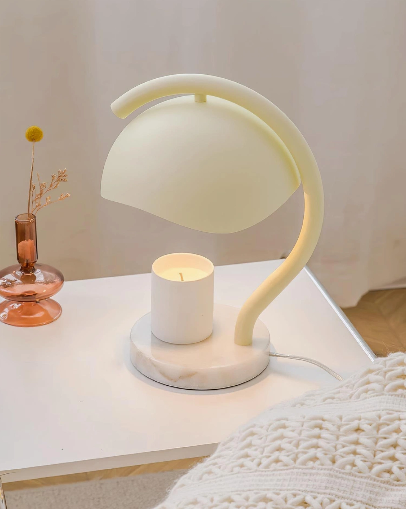 Minimalist candle warmer table lamp with white marble base and pillar candle on white side table with amber glass vase