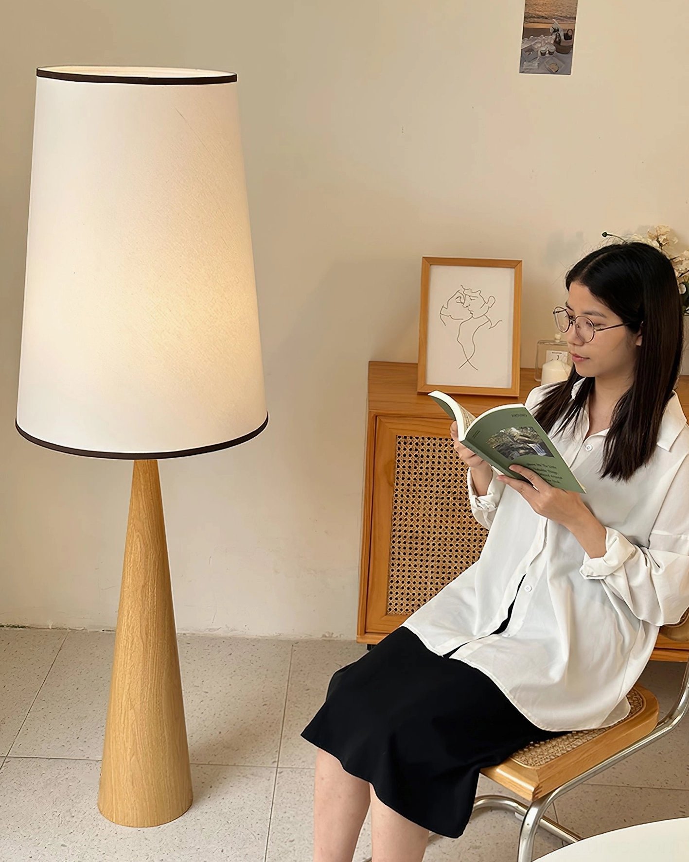 Light oak tapered floor lamp providing ambient reading light in cozy reading nook with woman reading nearby