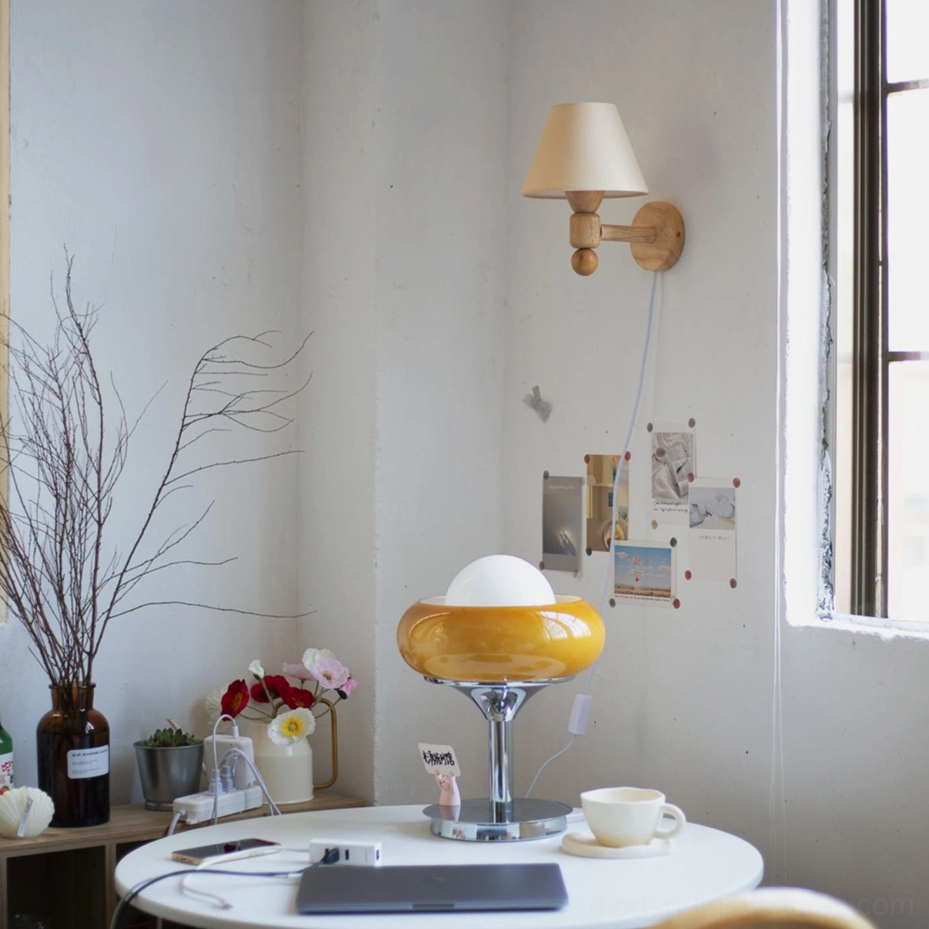 Contemporary hardwired wall lamp with beige shade mounted near dining area window with natural light and dried plants