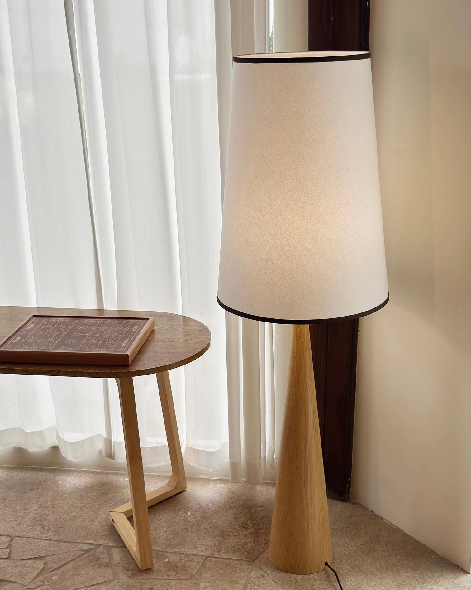 Tapered wooden floor lamp with neutral fabric shade next to round side table in modern interior corner