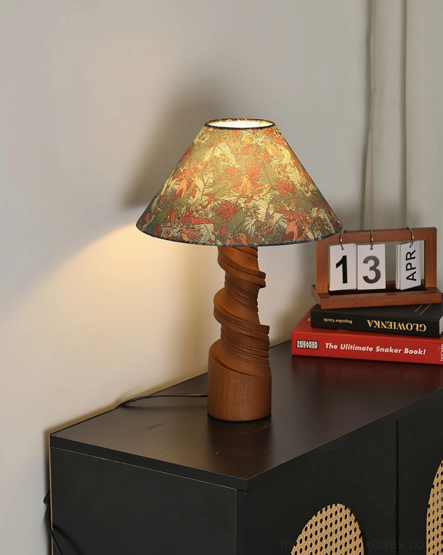 Scrollroot table lamp with floral printed shade on dark wood table, styled with calendar and book accessories