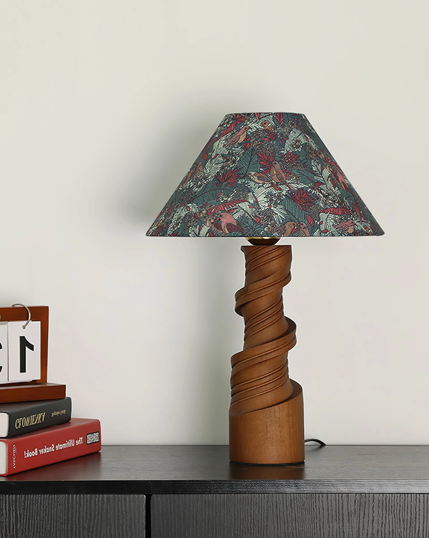 Scrollroot table lamp with floral printed fabric shade on dark wood table, styled with stacked books