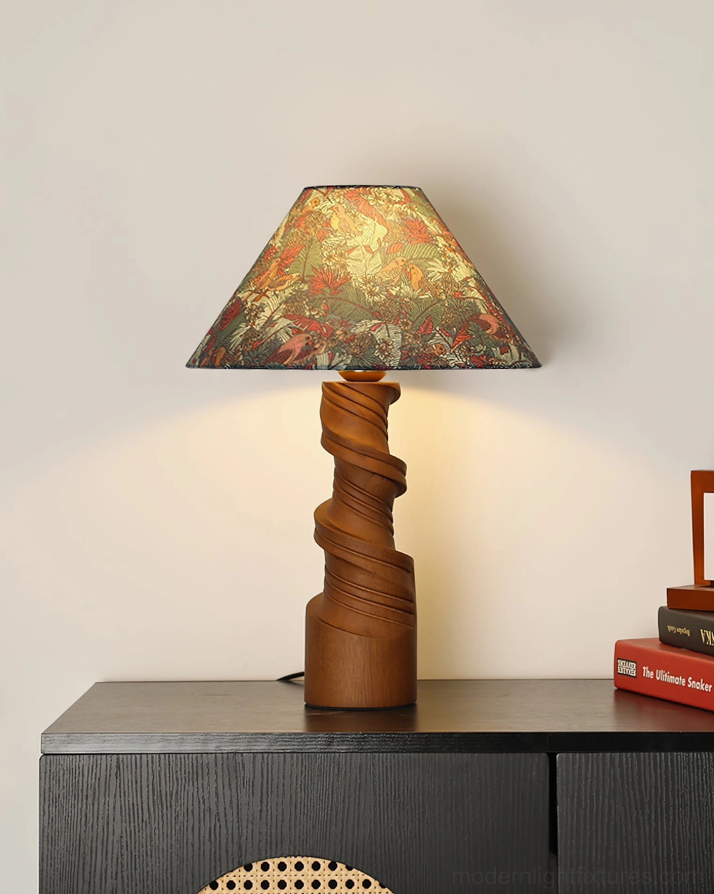 Scrollroot table lamp with floral fabric shade on dark wood side table, styled with books and decor elements
