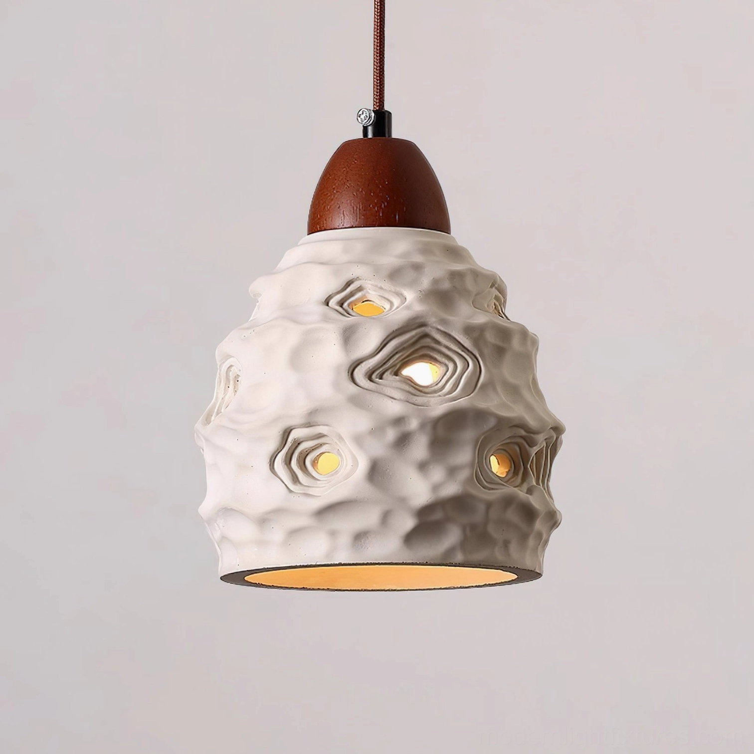 Sculptural ceramic pendant light with crater-like perforations creating artistic light diffusion pattern