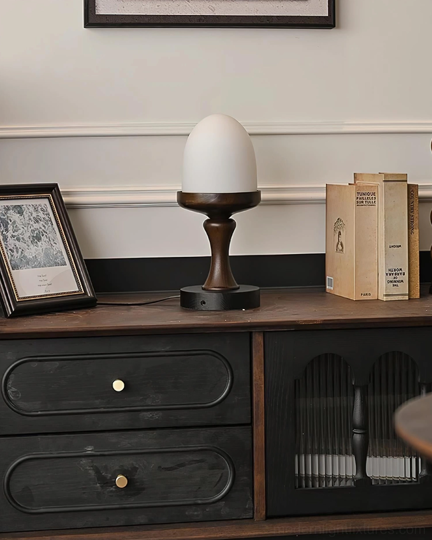 Contemporary organic table lamp unlit on retro console table with framed art and decorative books, three-quarter front