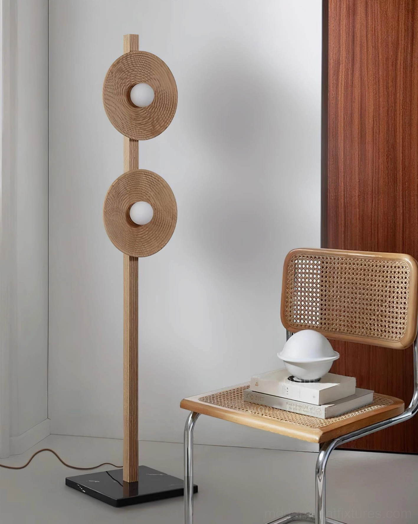 Twin disc floor lamp in reading corner with rattan chair and wooden wall panel warm minimalist setting