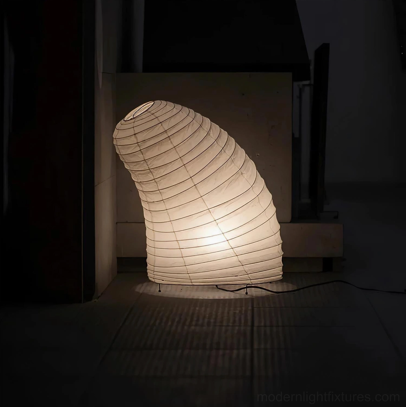 Sculptural paper lamp with soft glowing light side view dark interior fireplace setting
