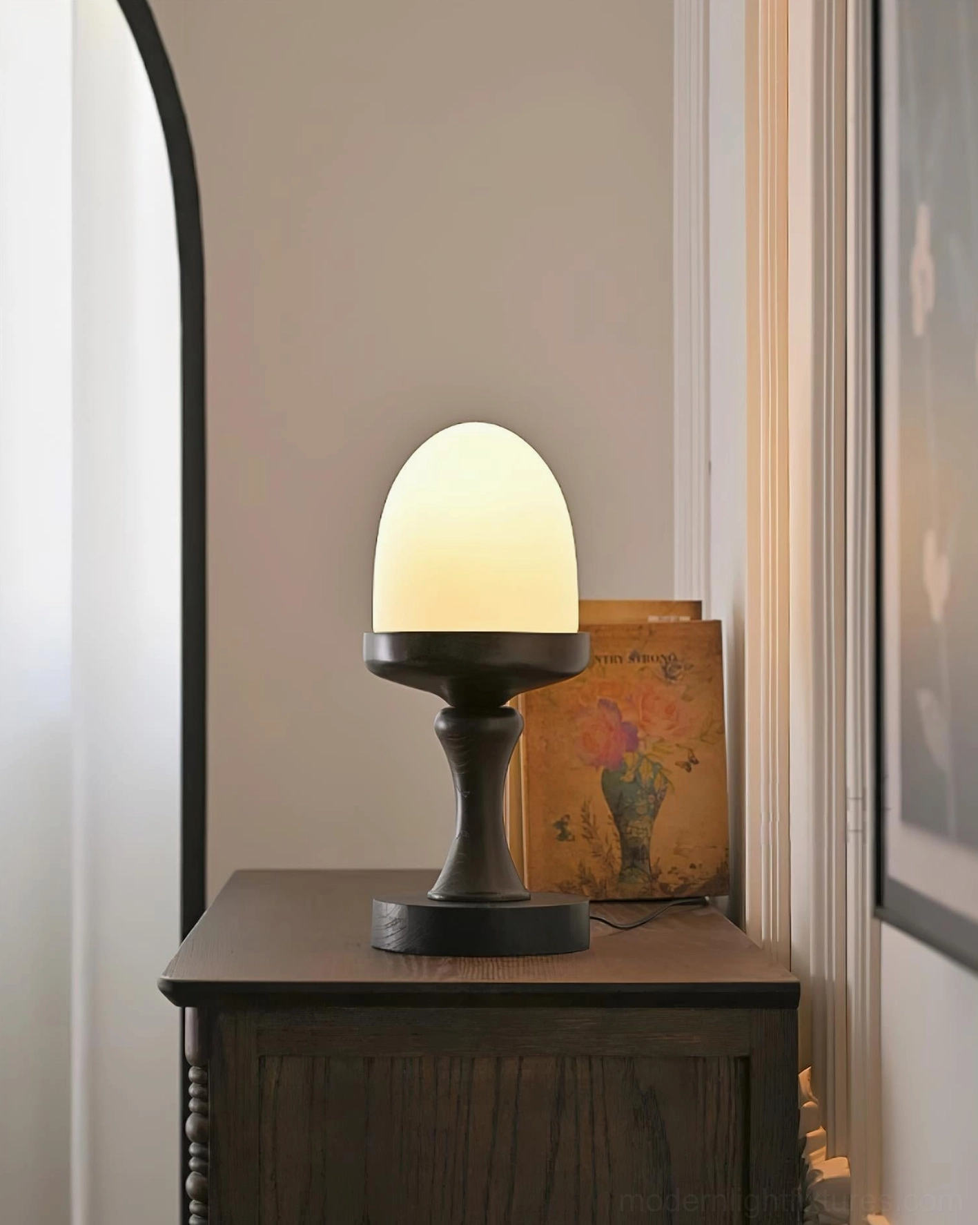 Contemporary egg lamp with warm glow on hallway side cabinet with vintage artwork, perspective view