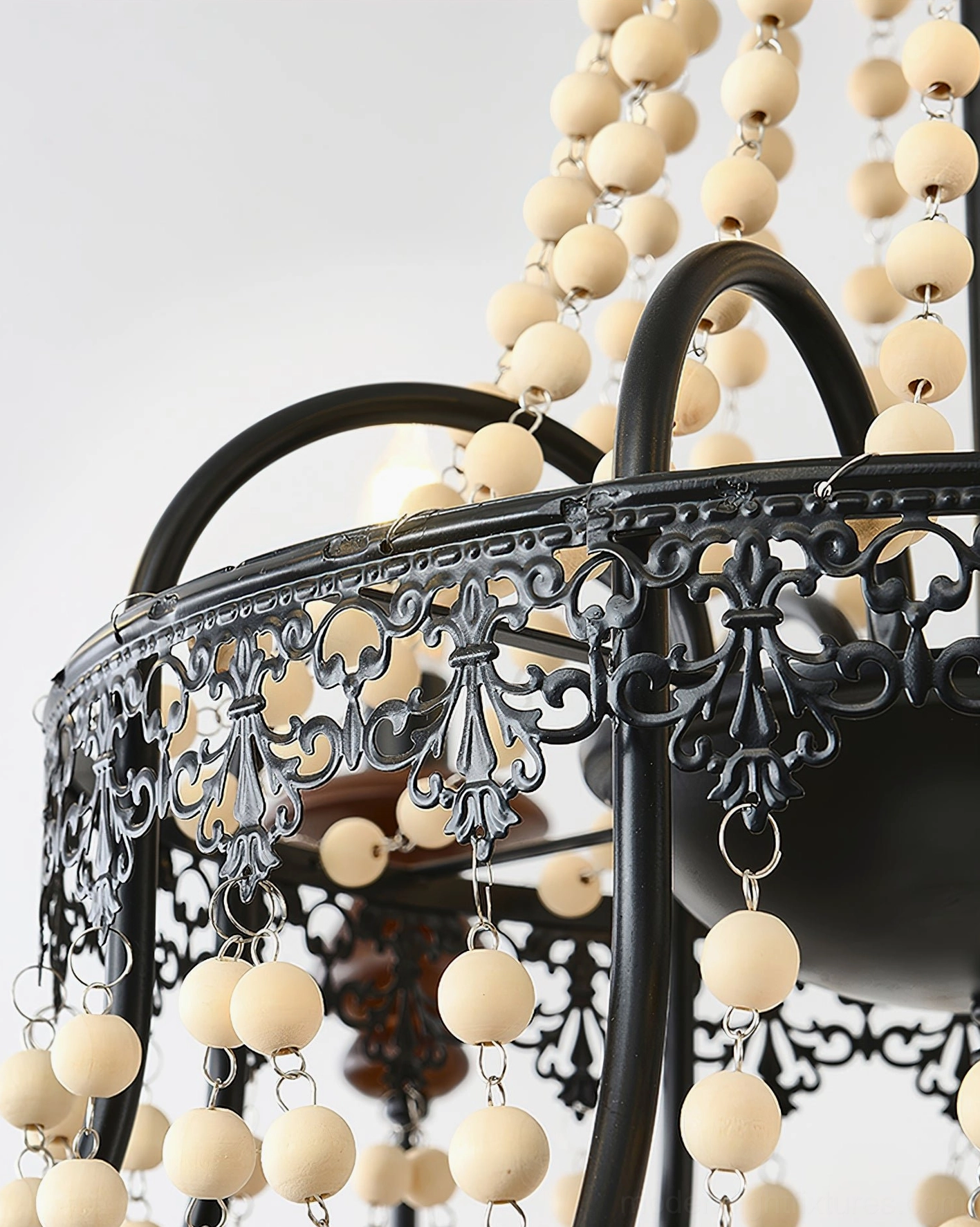 Seraphine beaded chandelier detail closeup highlighting hand-carved wooden candle caps, pearl bead tassels, and black iron craftsmanship