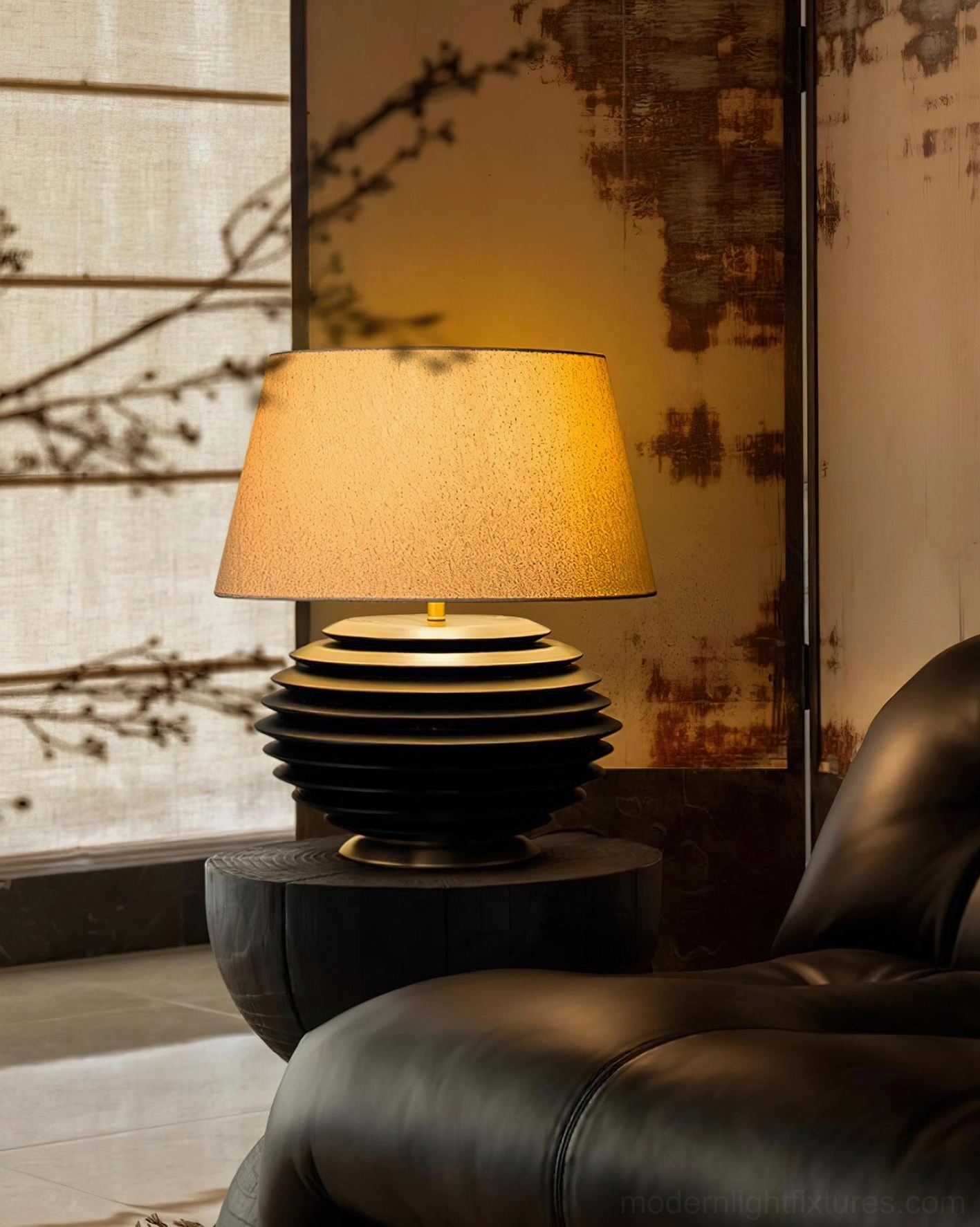 Serenity Strata table lamp with black ribbed base on round luxury side table, warm lit shade beside leather sofa, upscale interior design