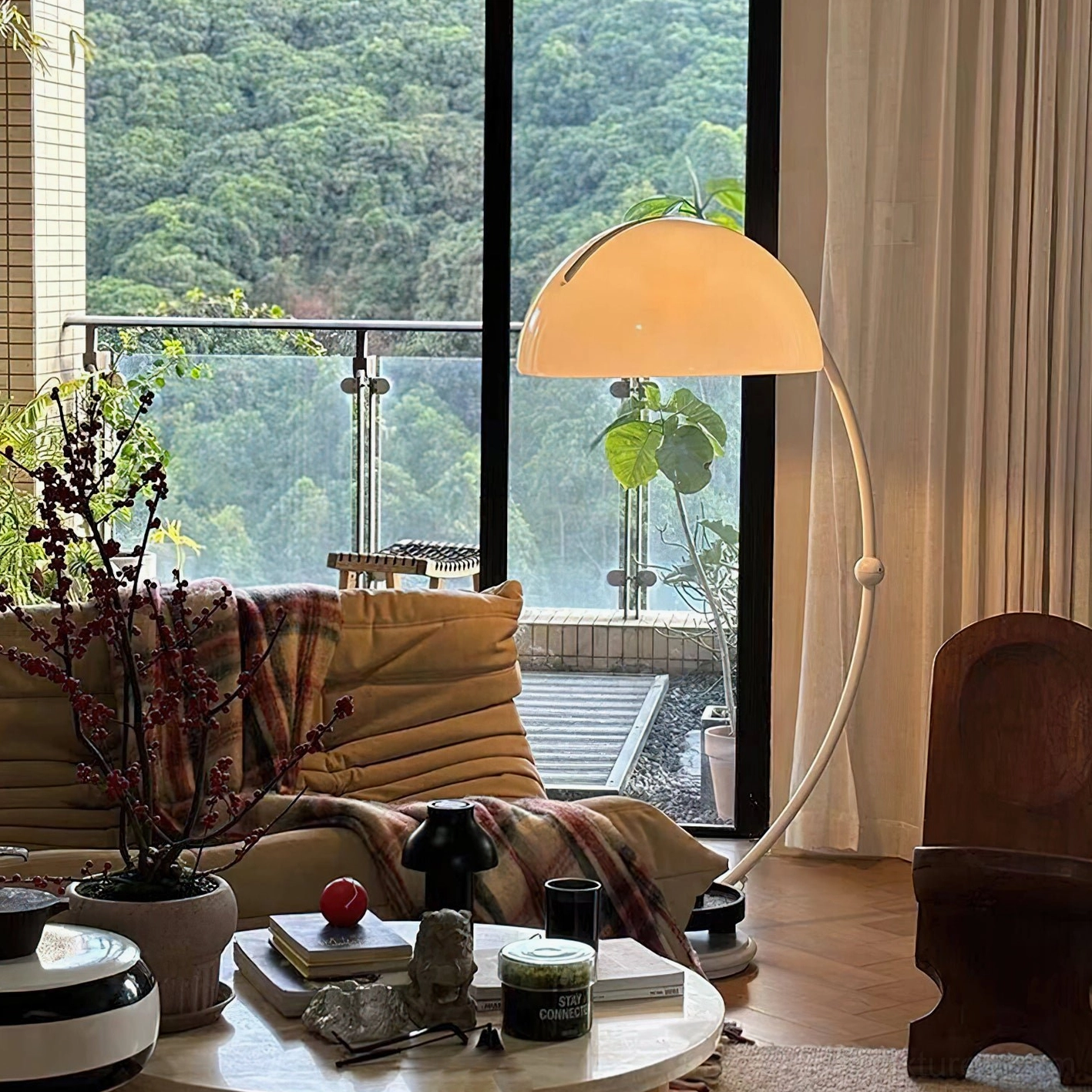 Warm-toned Serpente rotating floor lamp on balcony lounge beside brown sofa with green outdoor view