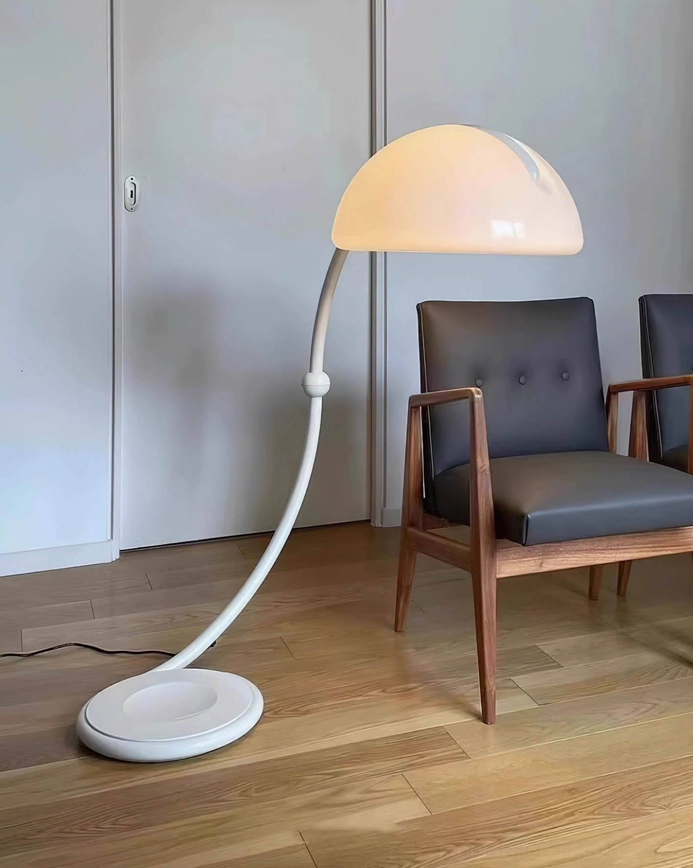 White Serpente dome floor lamp beside wooden armchair with dark cushion