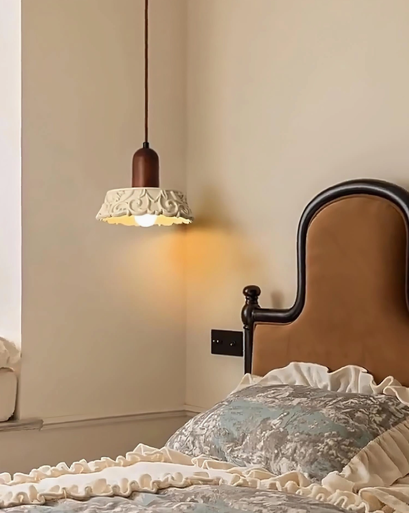 Carved resin pendant lamp creating warm ambiance in cozy vintage bedroom with brown wooden headboard