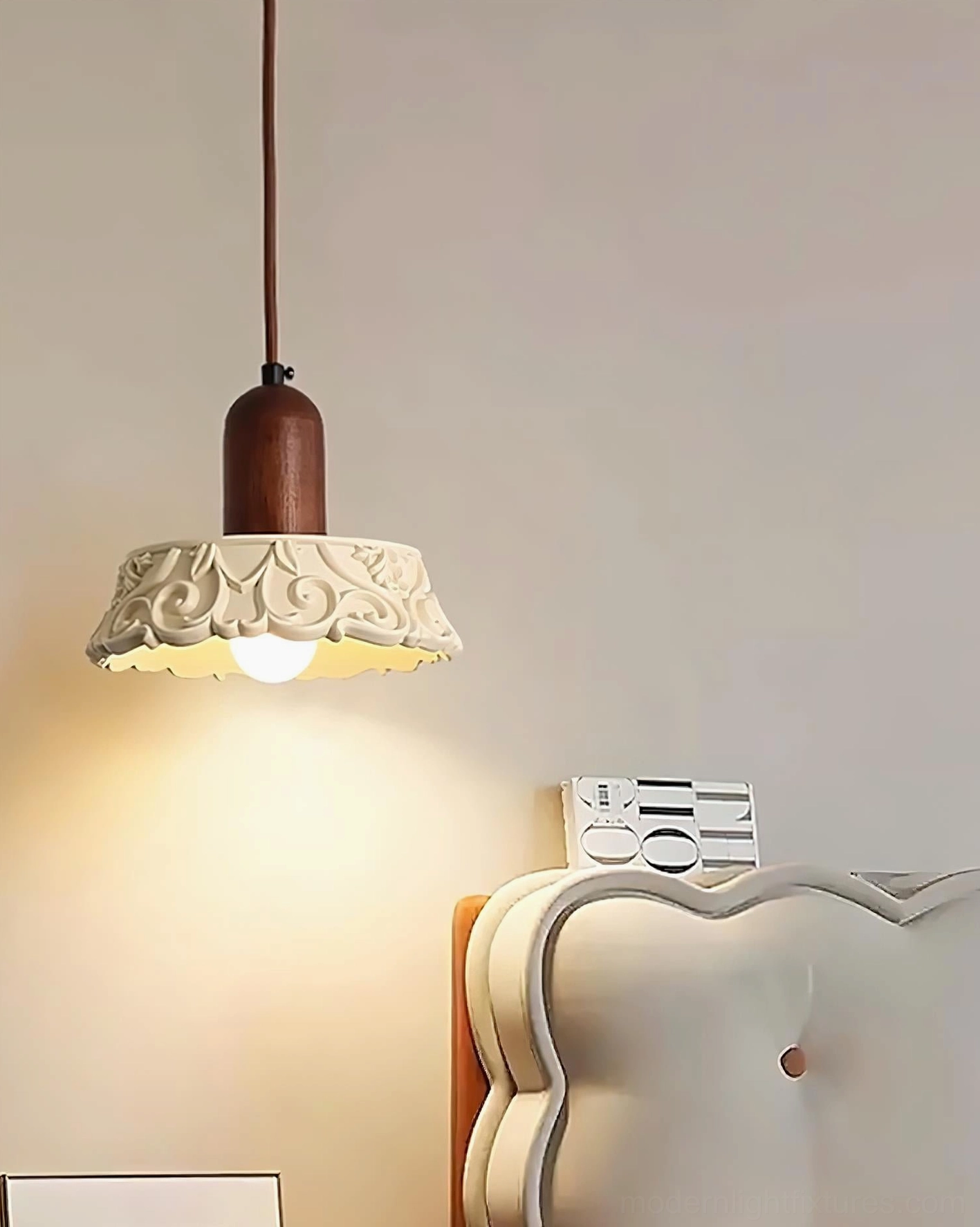Hand-carved resin pendant lamp with walnut wood fixture glowing above white tufted headboard, three-quarter front view