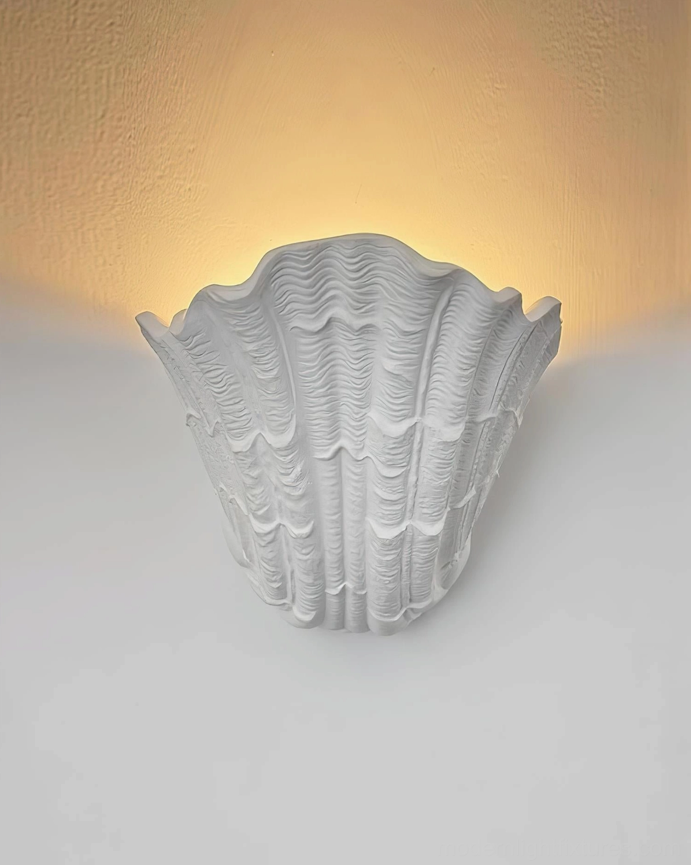 Shell-shaped plaster wall sconce mounted indoors with ambient warm glow and soft diffused illumination