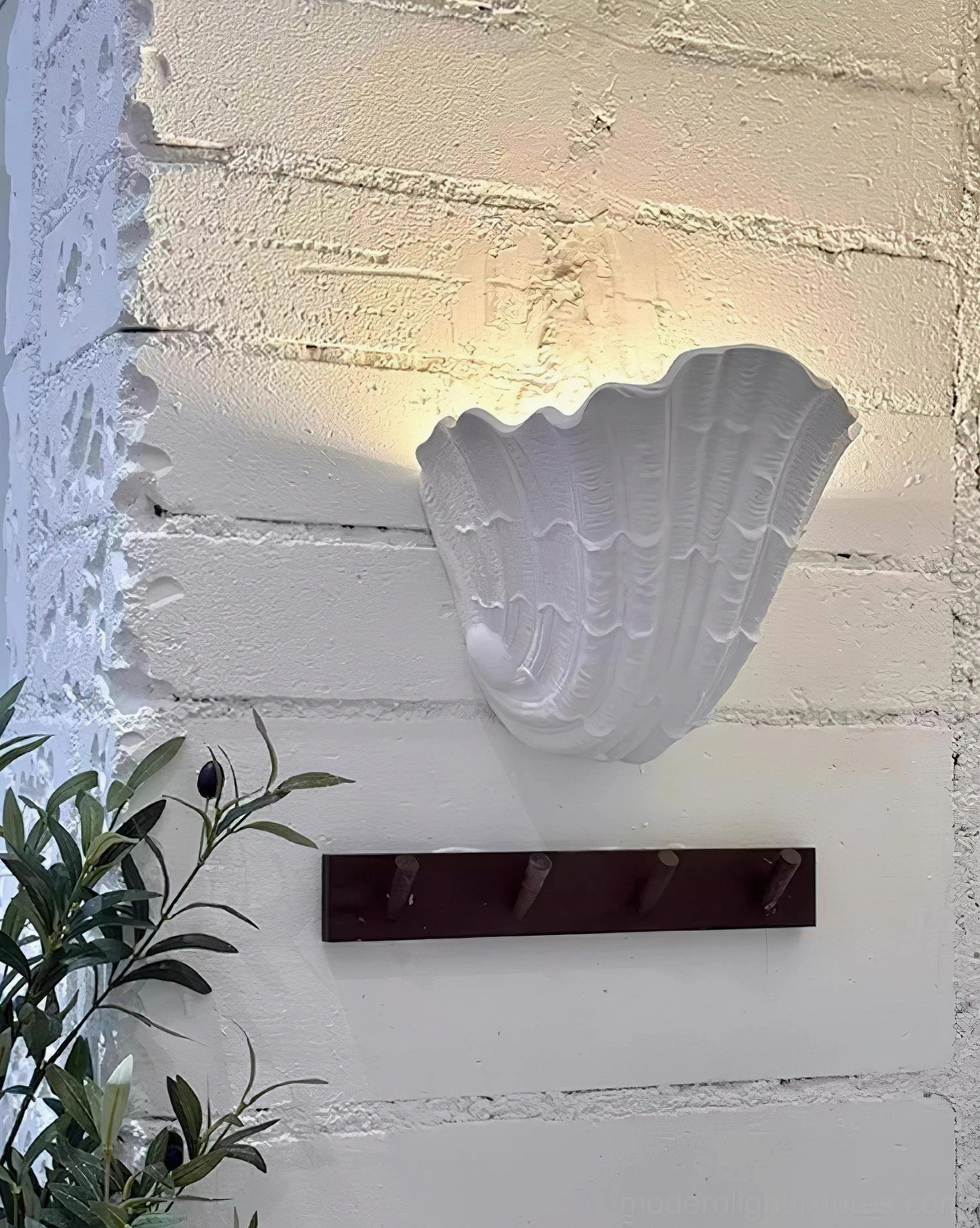 Shell plaster wall sconce side profile mounted on exposed brick wall with warm glowing light and coat rack below