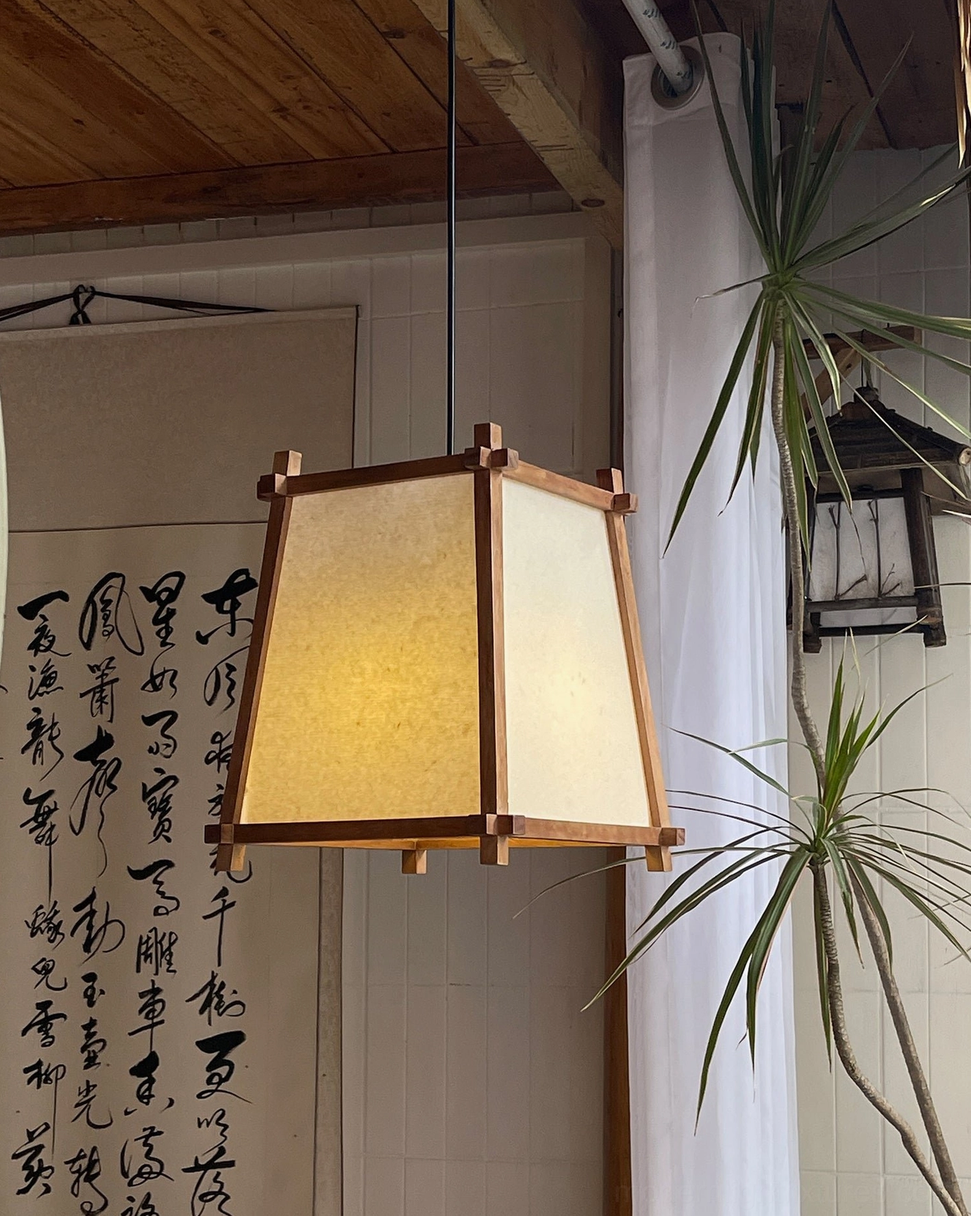 Trapezoidal pendant light three-quarter view with warm ambient glow and calligraphy wall art backdrop