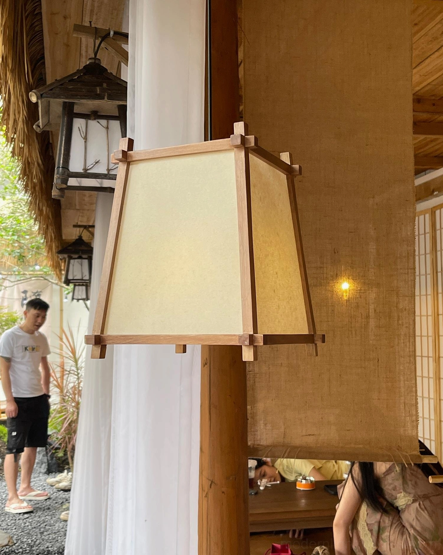 Geometric wood pendant lamp in patio teahouse setting with natural outdoor lighting and thatched roof