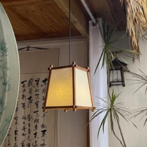 Geometric wood pendant lamp hanging in traditional teahouse with parchment fabric shade and tropical greenery