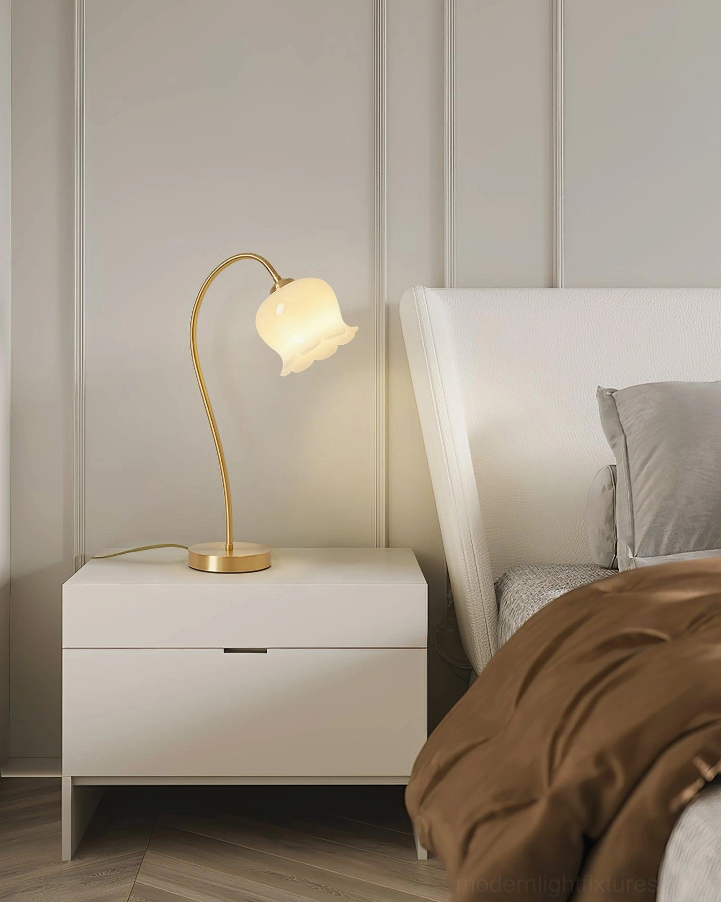 Brass lily table lamp on white nightstand in minimalist bedroom, bedside lighting creating warm glow