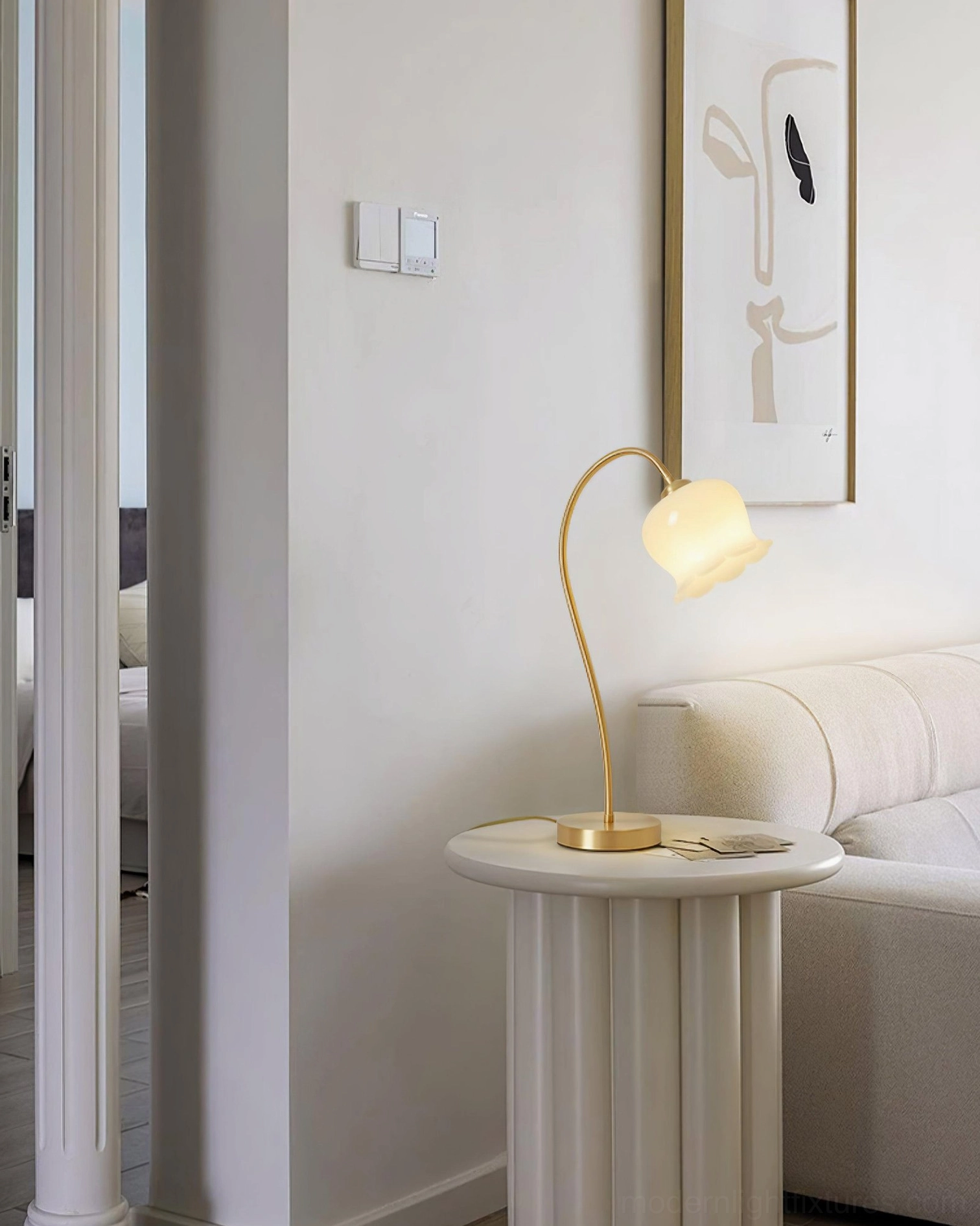 Side view of modern brass table lamp on round accent table in minimalist living space with wall art