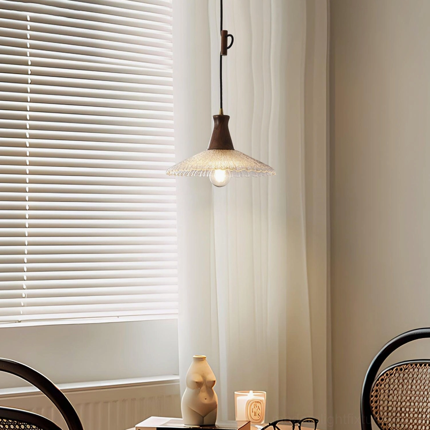 Small-scale walnut and clear glass pendant light in minimalist dining space with window treatments