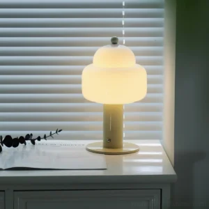 Soreli beige metal table lamp with frosted glass shade and green finial on home desk with window blinds
