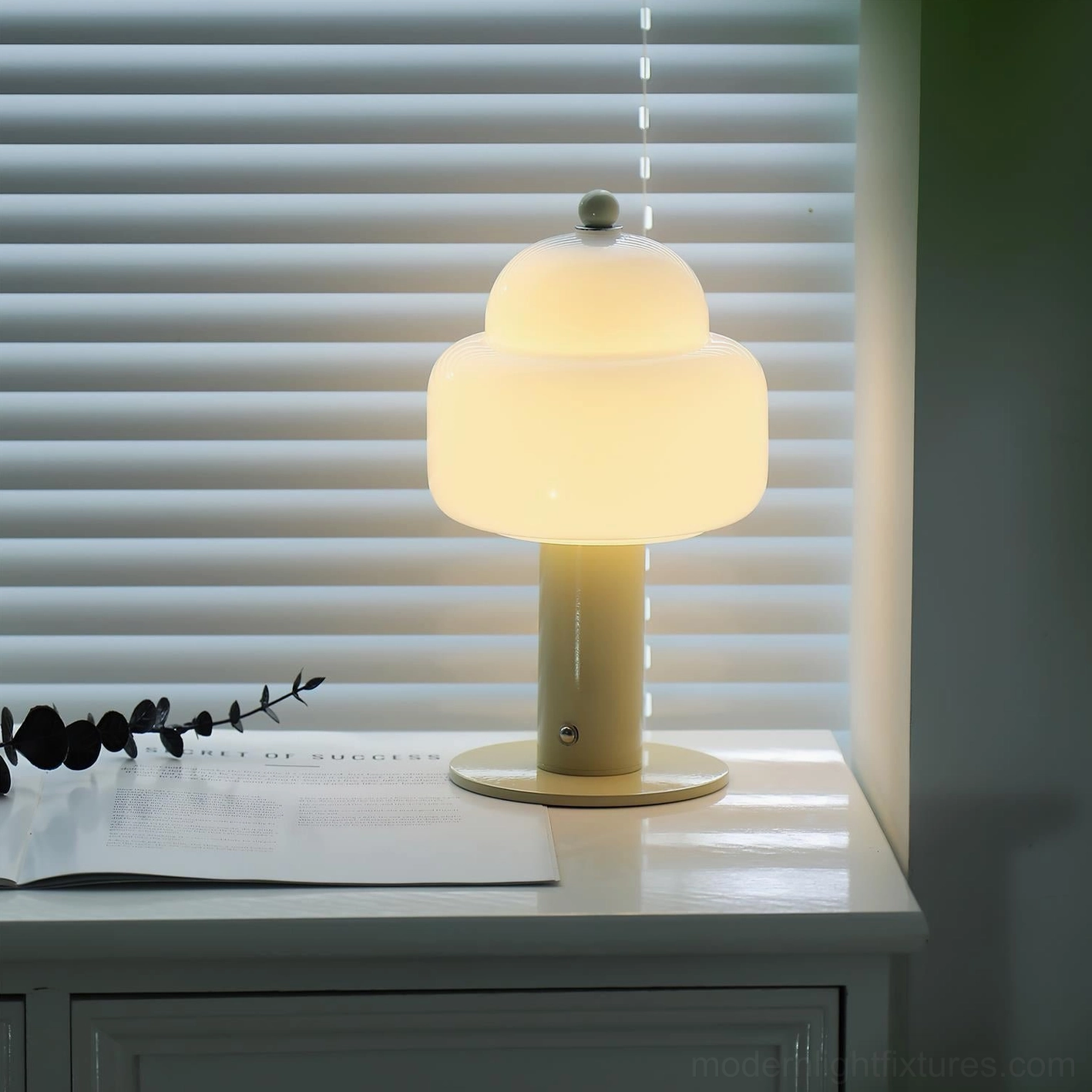 Soreli beige metal table lamp with frosted glass shade and green finial on home desk with window blinds