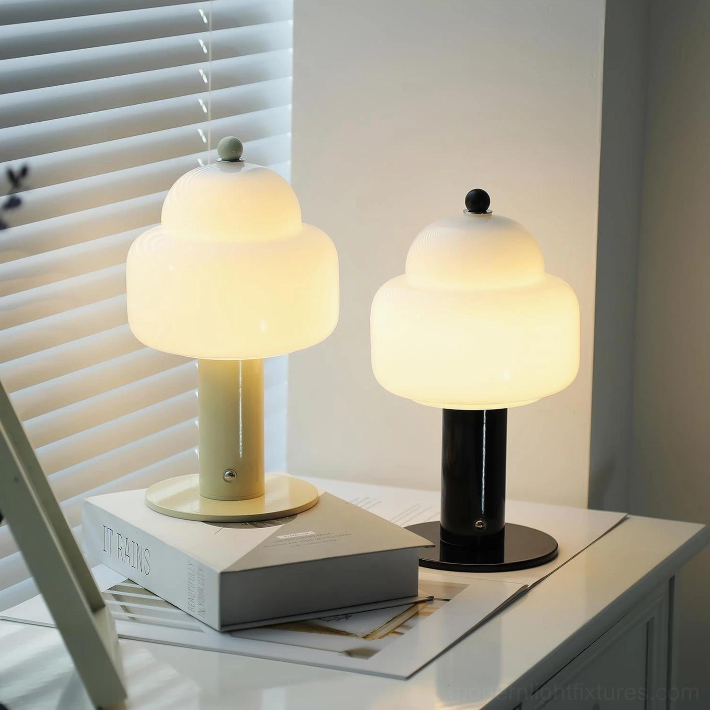 Two Soreli table lamps in black and beige variants on home study desk with books and window blinds