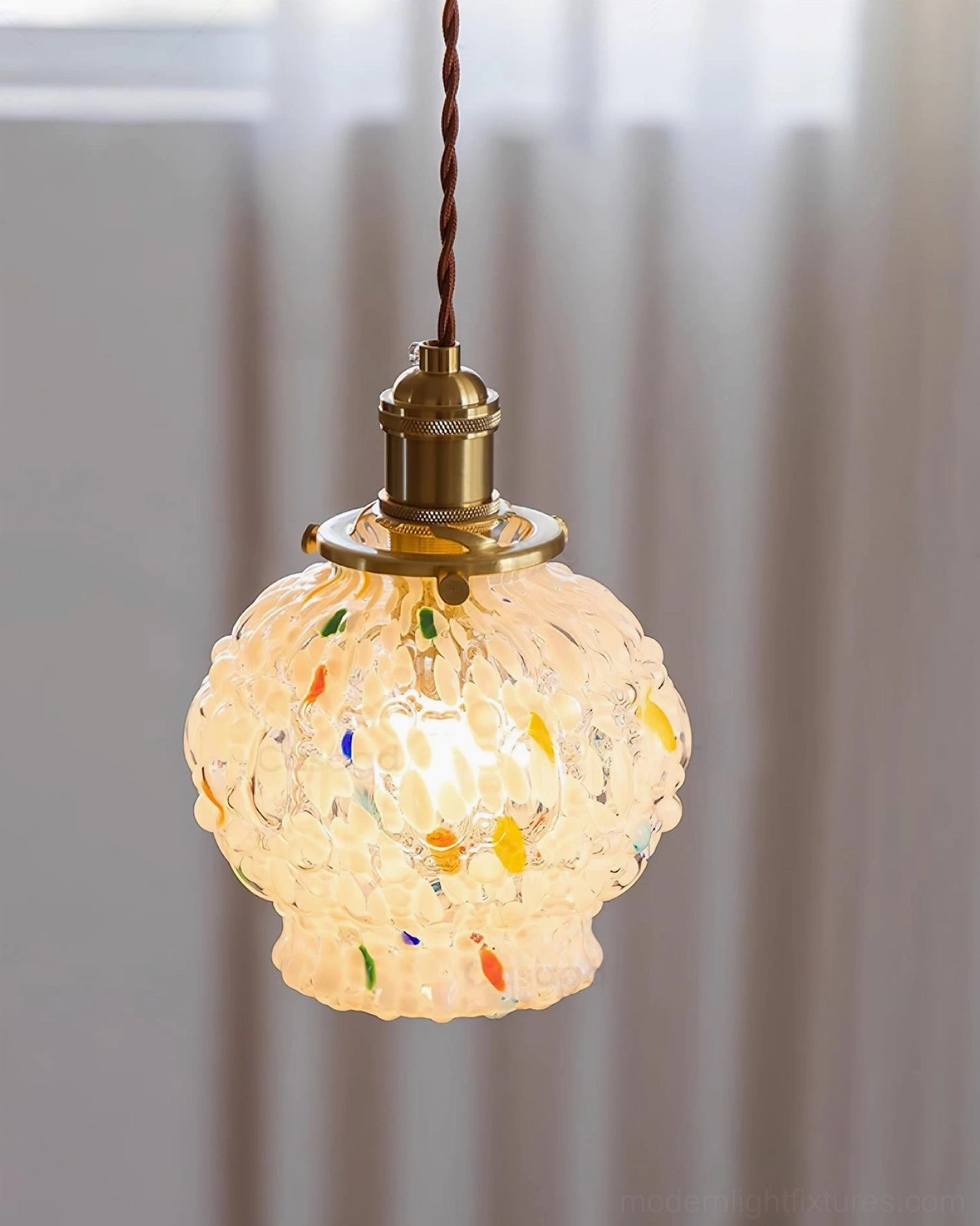 Lit confetti glass pendant lamp creating warm ambient light, frosted shade with speckles, contemporary interior with sheer curtains
