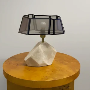 Modern geometric table lamp placed on wooden side table, three-quarter view showing travertine base detail