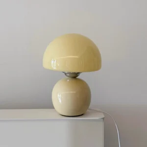 Modern Spika table lamp with warm beige glossy finish displayed on white shelf with minimalist backdrop