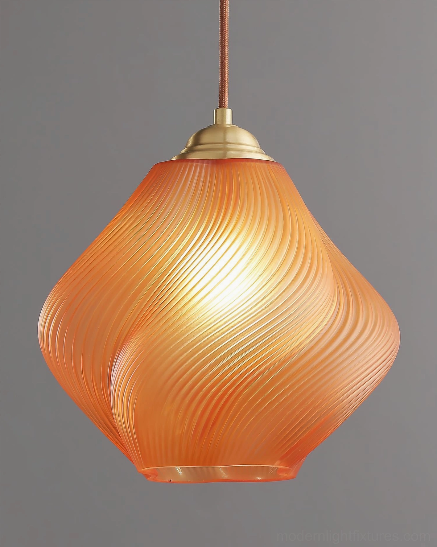 Spirvia twisted glass pendant light in amber - warm glowing interior light detail shot with brass metal components and gray studio background