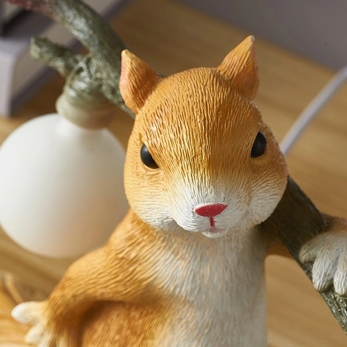 Close-up front view of squirrel table lamp highlighting orange-white resin craftsmanship and round bulb
