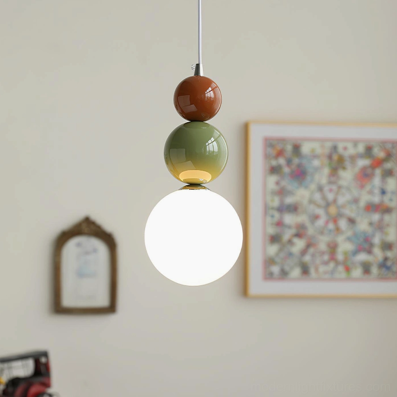 Close-up of three-sphere pendant light showing frosted white globe with terracotta and sage green accent colors