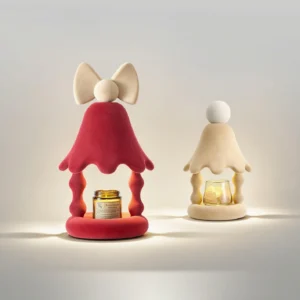 Two Stacy candle warmer lamps in red and beige finishes, flat lay comparison view with glowing candles inside, minimalist studio setting