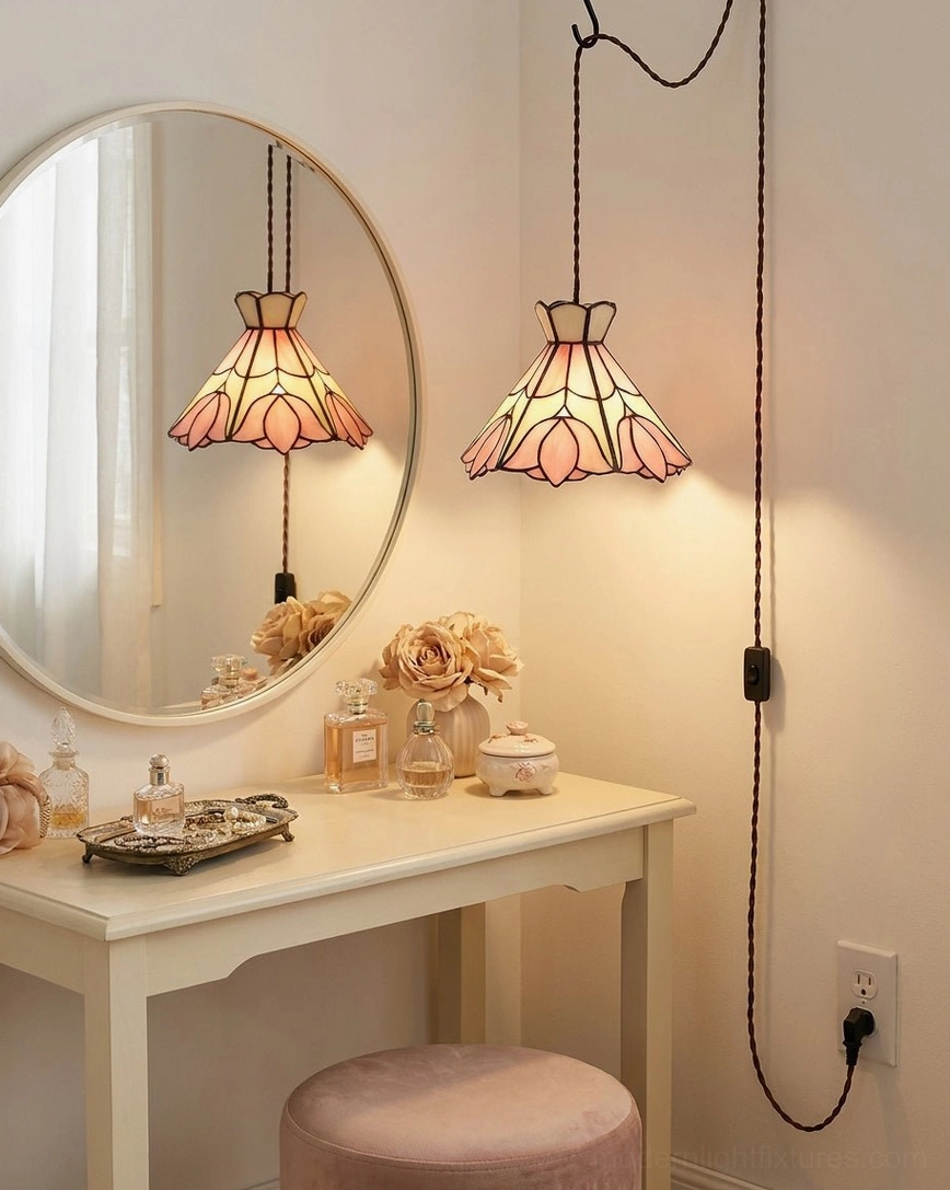 Stained glass pendant light hung above vanity mirror in makeup area, pink and cream lotus shade with copper-foil seams reflected in round mirror
