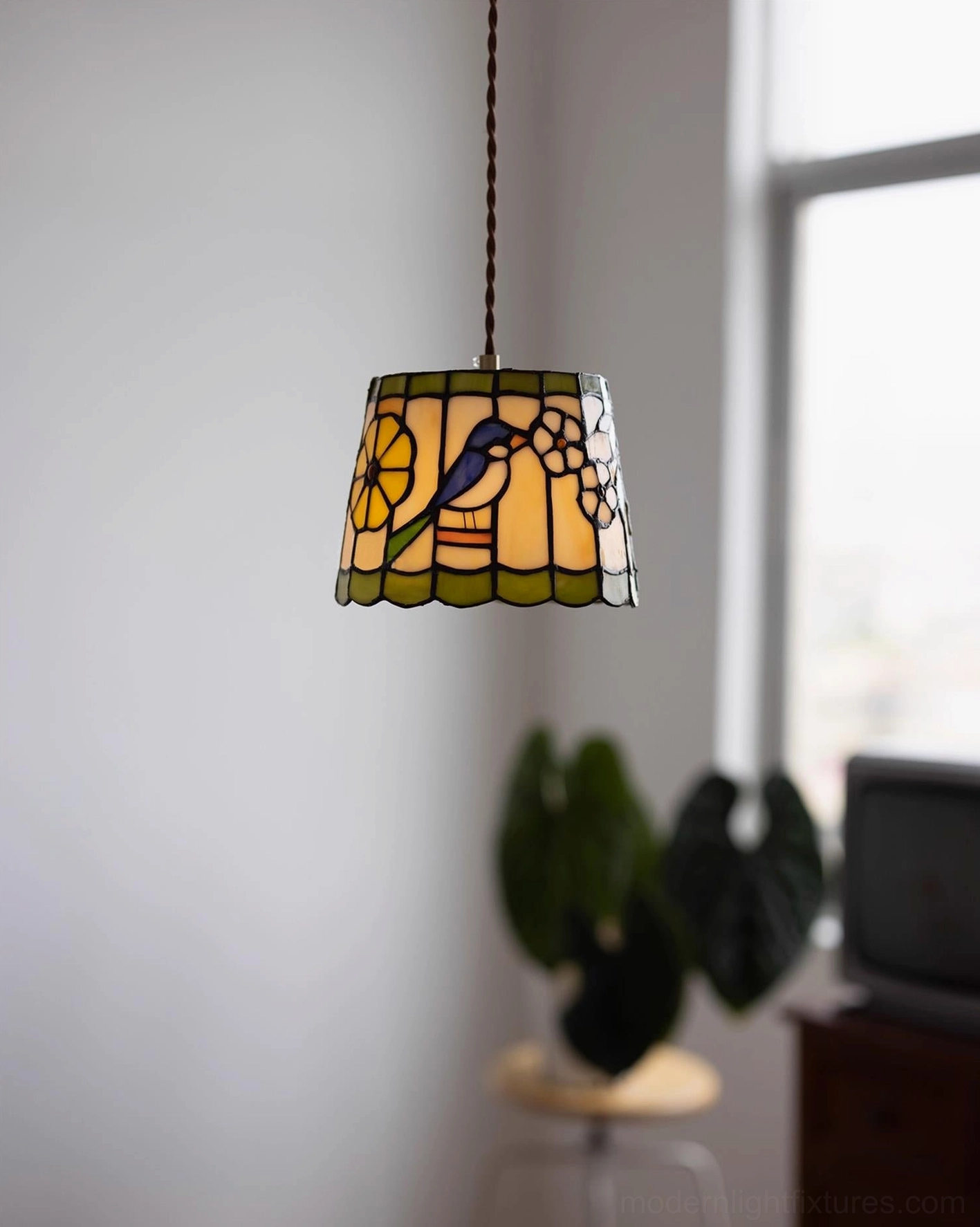 Warm-toned stained glass pendant light with hand-crafted bird and floral motif in bedroom setting